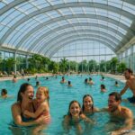 Panoramabad Pforzheim in moderner Hallenbad-Optik mit vielen Badegästen unter einem großen Glasdach; unten rechts steht zwischenkaffeeundkant.de.